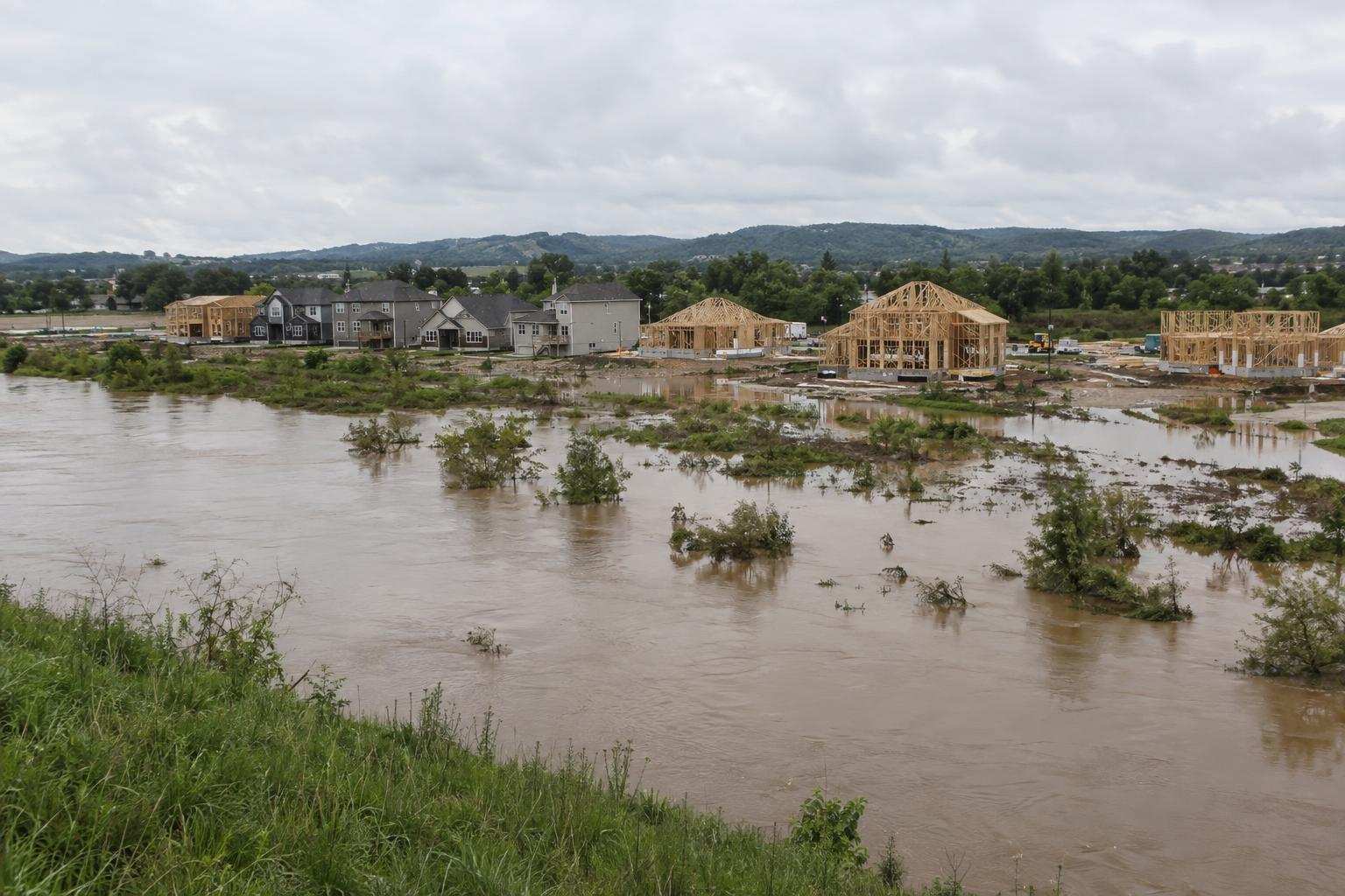Finished homes and houses under construction beside flooded lots near a swollen river.